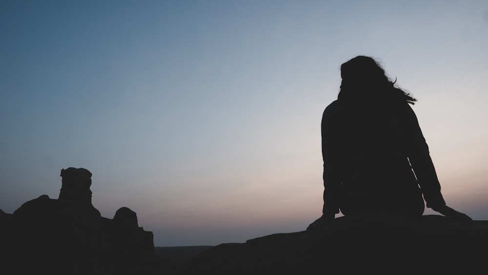 silhouette d’homme debout sur le rocher pendant le coucher du soleil