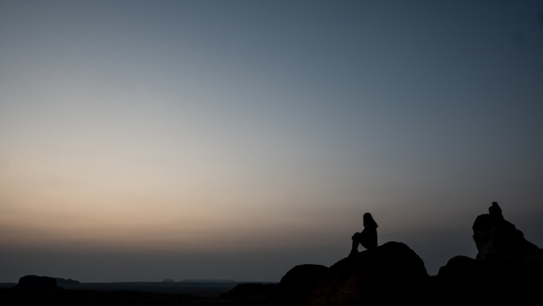 silhouette of person sitting on rock during sunset