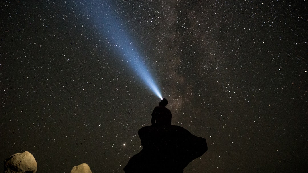 silhouette of man sitting on rock under starry night