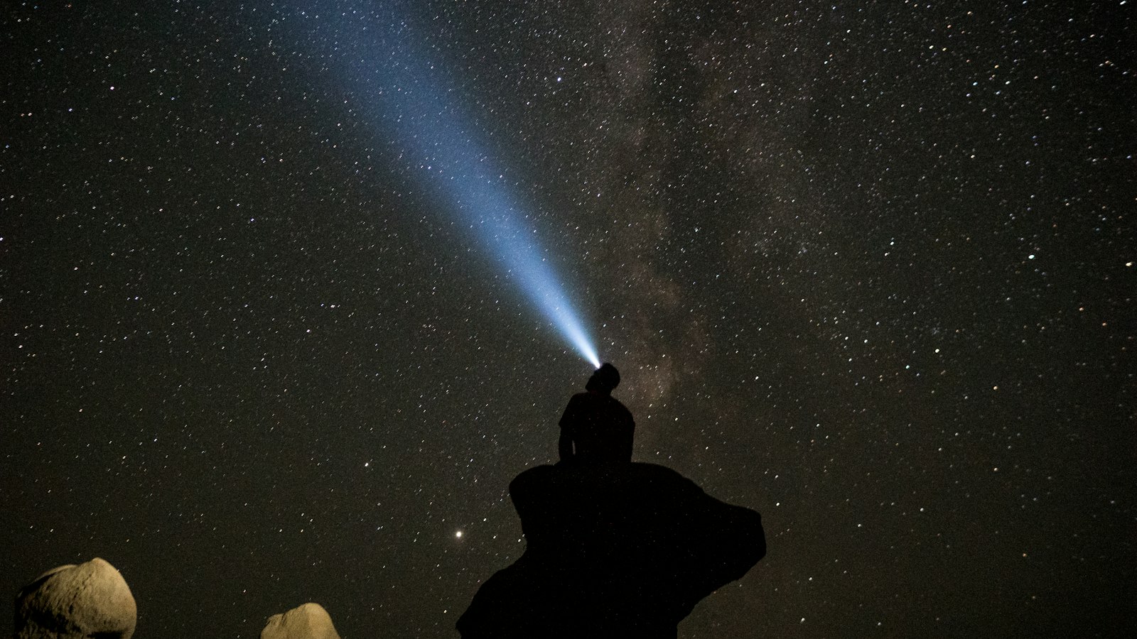 Une silhouette éclaire le ciel étoilé avec une lampe frontale