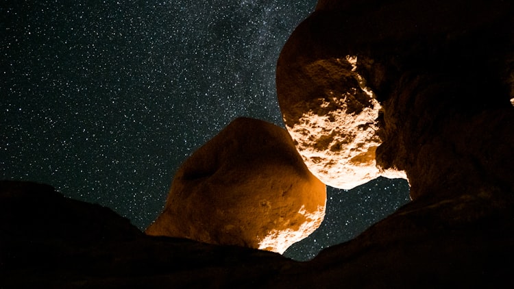 Two yellow rocks lit from below, with a starry night sky behind them