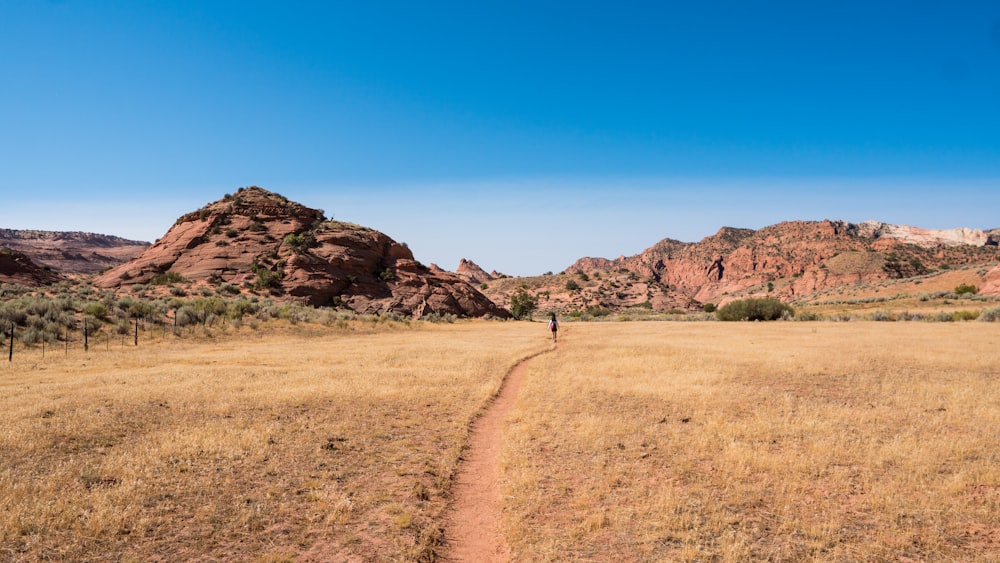 brown dirt road near brown mountain under blue sky during daytime