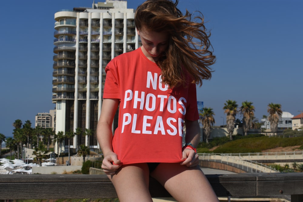 woman in red and white crew neck t-shirt sitting on brown wooden bench during daytime