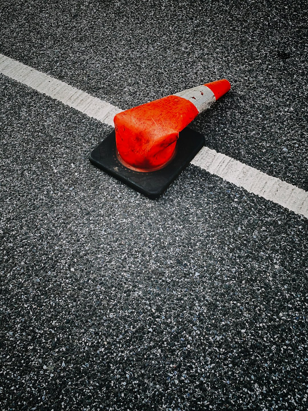 orange and white traffic cone on black and white asphalt road