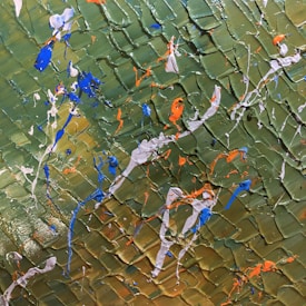 An abstract painting with a textured background featuring olive green tones. Bright splashes and drips of vivid blue, orange, and white paint are scattered across the surface, creating an energetic and dynamic composition.