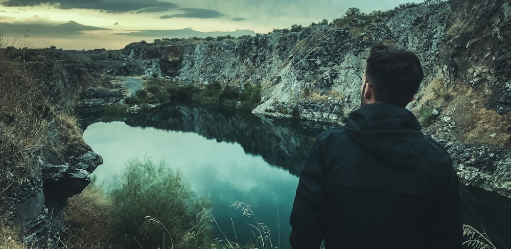 man in black hoodie standing near lake during daytime