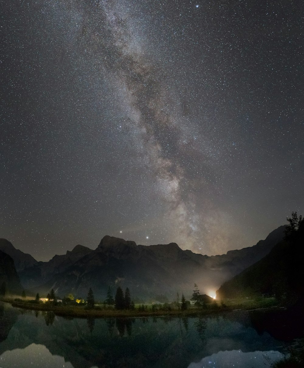 body of water near trees and mountain under starry night