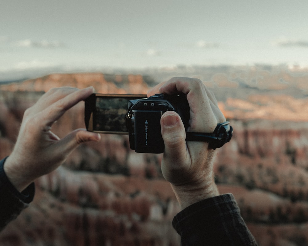 昼間、黒いスマートフォンを手にした人が茶色の野原の写真を撮る