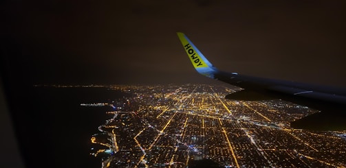 Nighttime cityscape viewed from an airplane window, bathed in soft blue light.