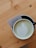 A cup of matcha latte with an intricate leaf pattern created in the foam, placed on a light wooden table. Beside the cup, a business card with the text 'L'ESTRADE POPULAIRE' is partially visible.