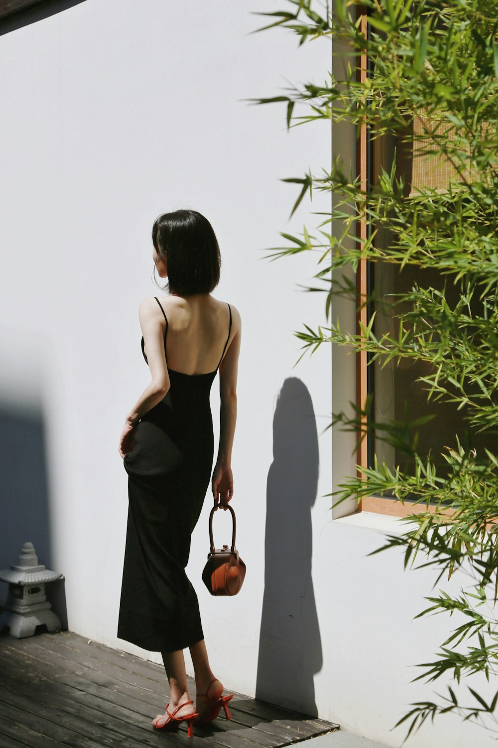 woman in black spaghetti strap dress holding brown leather sling bag