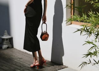 woman in black spaghetti strap dress holding brown leather sling bag