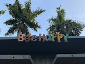 Colorful letters spelling 'Be Happy' are mounted on a structure, with palm trees in the background against a clear blue sky.