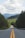 gray concrete road between green trees under white clouds and blue sky during daytime
