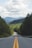 gray concrete road between green trees under white clouds and blue sky during daytime