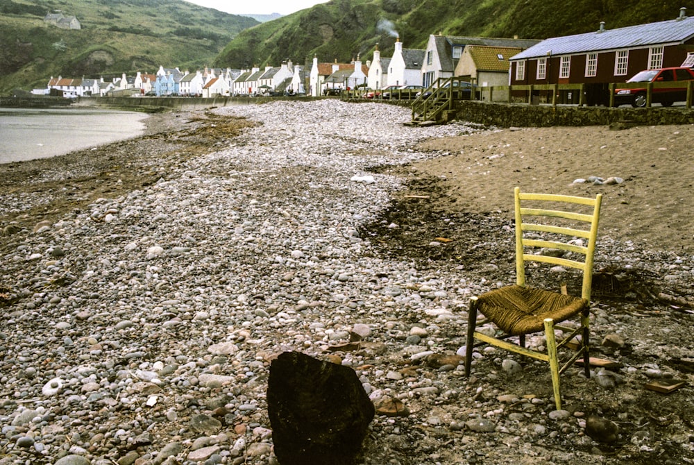 brown wooden armchair on gray sand near body of water during daytime