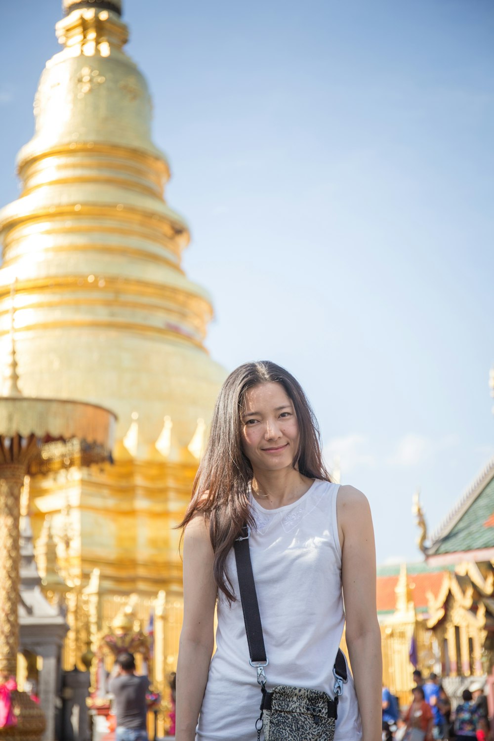 Mujer con camiseta blanca sin mangas de pie cerca de la torre dorada