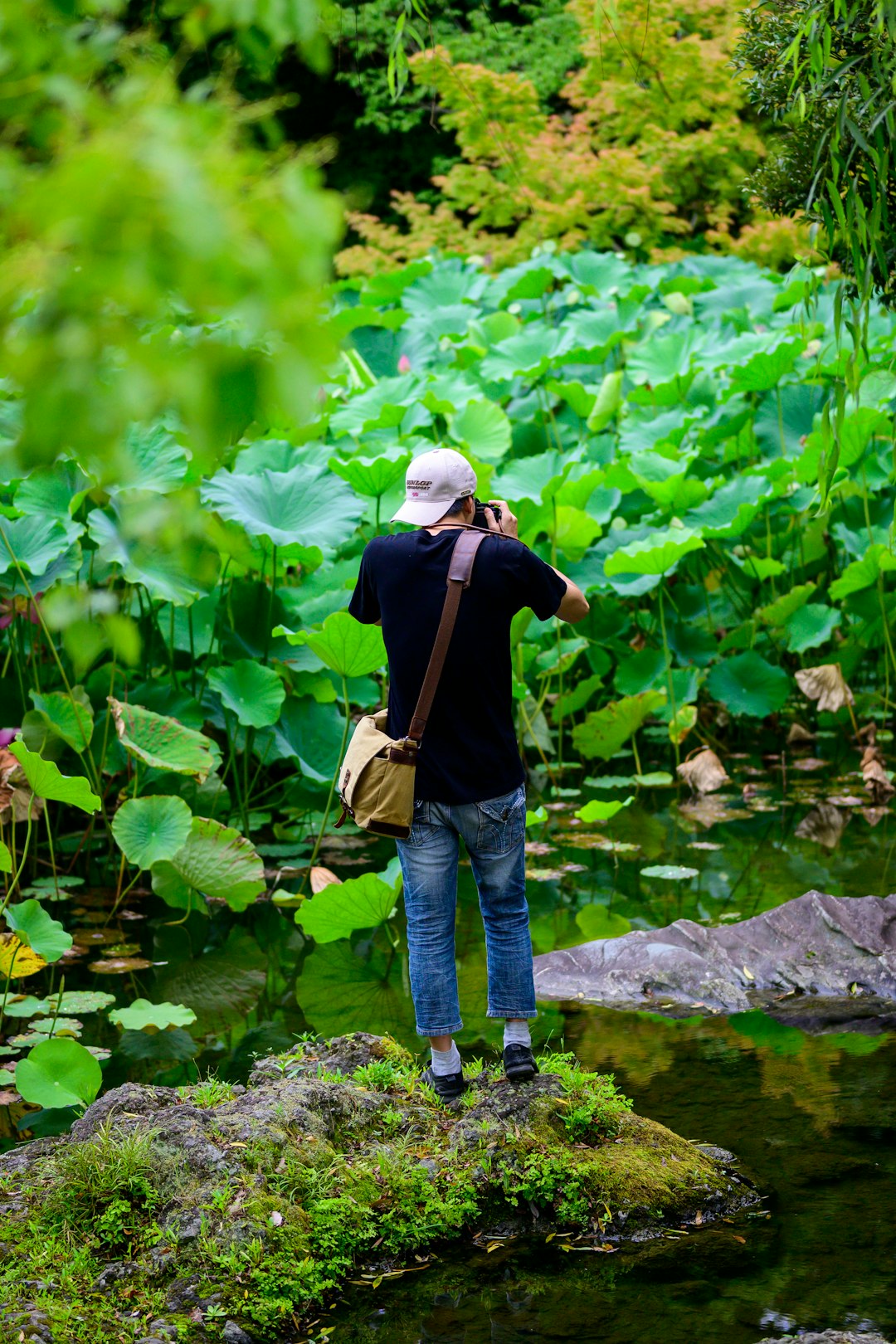 man in black jacket and blue denim jeans standing on rock near river during daytime