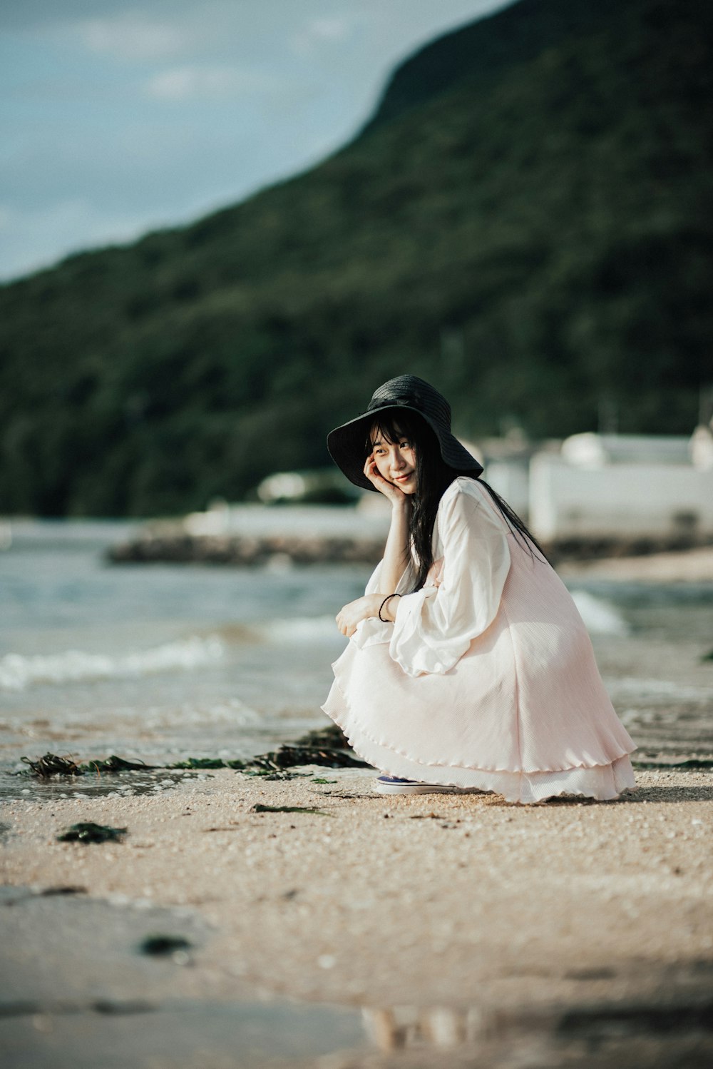 woman in white dress and black hat sitting on beach shore during daytime