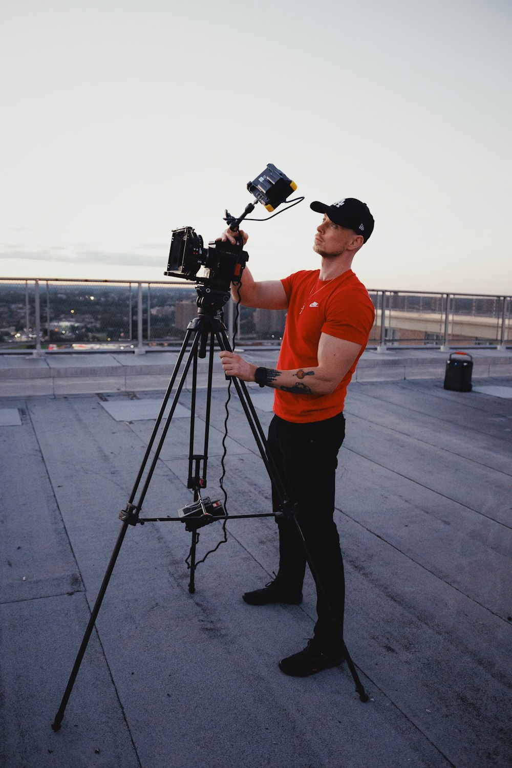man in orange t-shirt and black pants holding black dslr camera