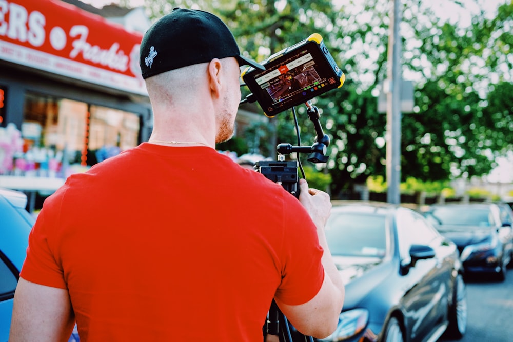 man in red crew neck t-shirt holding black smartphone