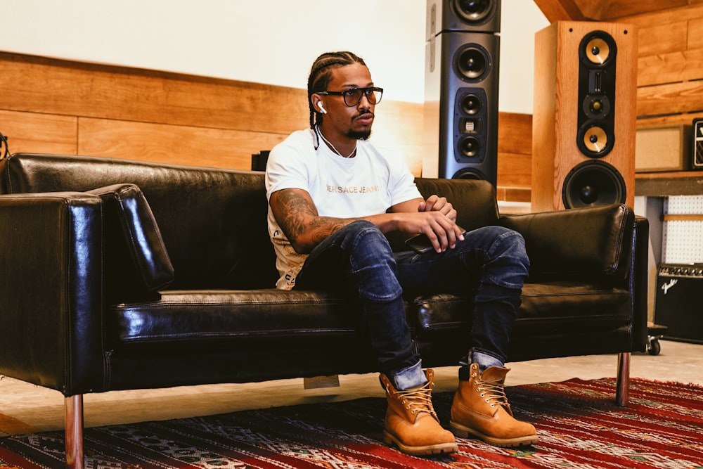 man in white polo shirt and blue denim jeans sitting on black leather couch