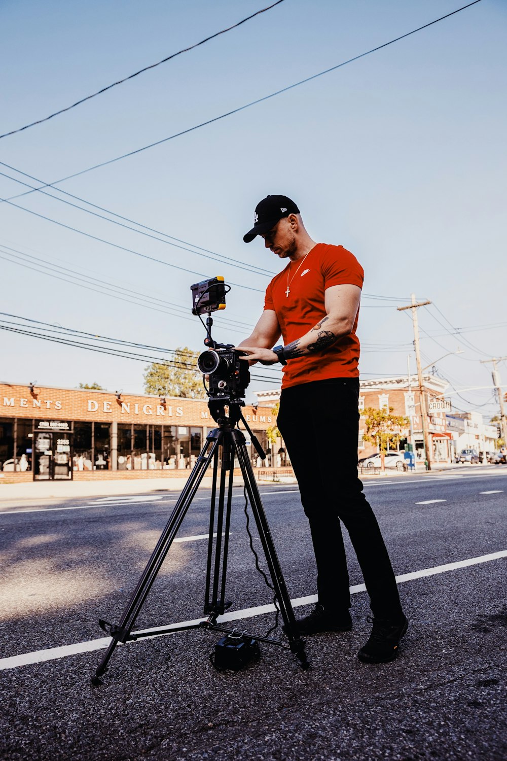 man in orange shirt and black pants holding camera standing on road during daytime
