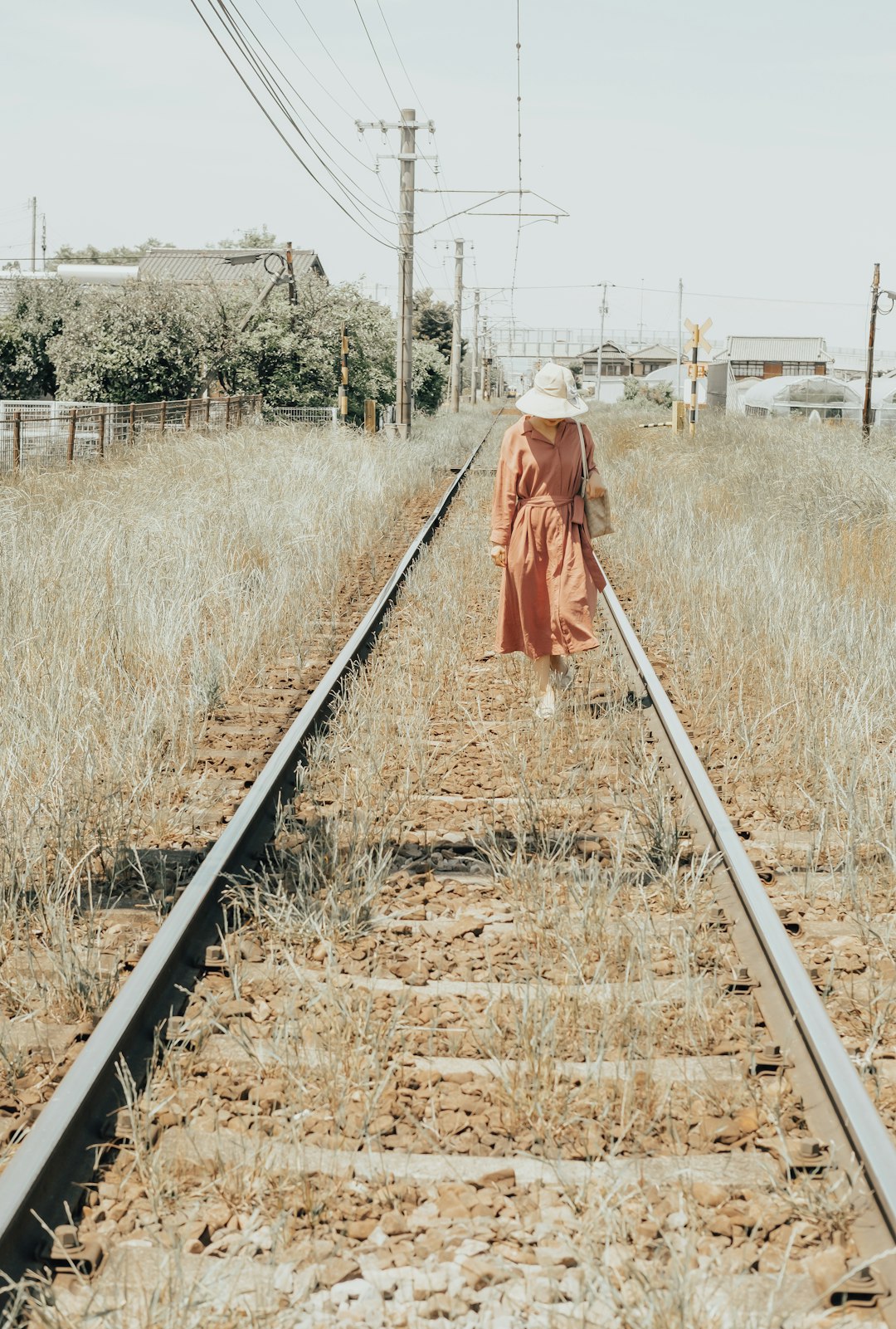 woman in red coat walking on train rail during daytime