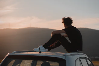 man in black long sleeve shirt sitting on car hood during daytime