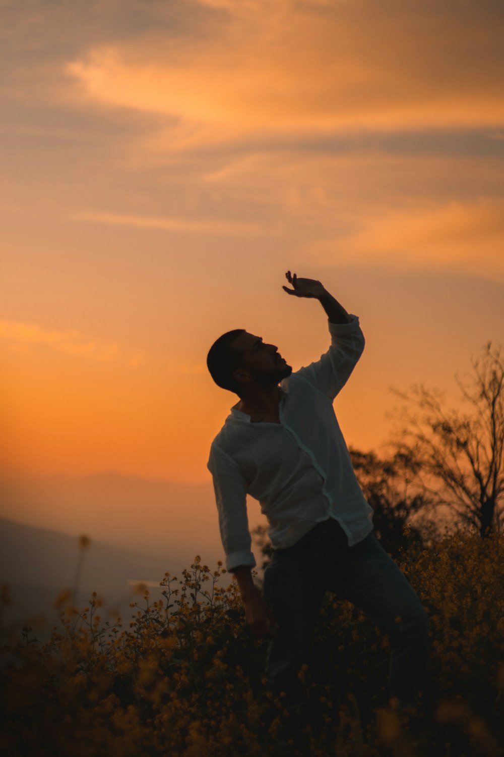 man in white dress shirt and black pants standing on grass field during sunset