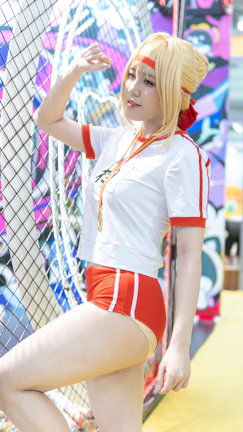Model wearing a red New Stance t-shirt with a bold American football graphic, standing by a stadium fence.