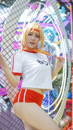 A person in a sporty outfit is posing in front of a colorful, graffiti-covered wall. They are wearing a white and red athletic attire with shorts, and they have a medal around their neck. The background is vibrant and filled with abstract designs and shapes.