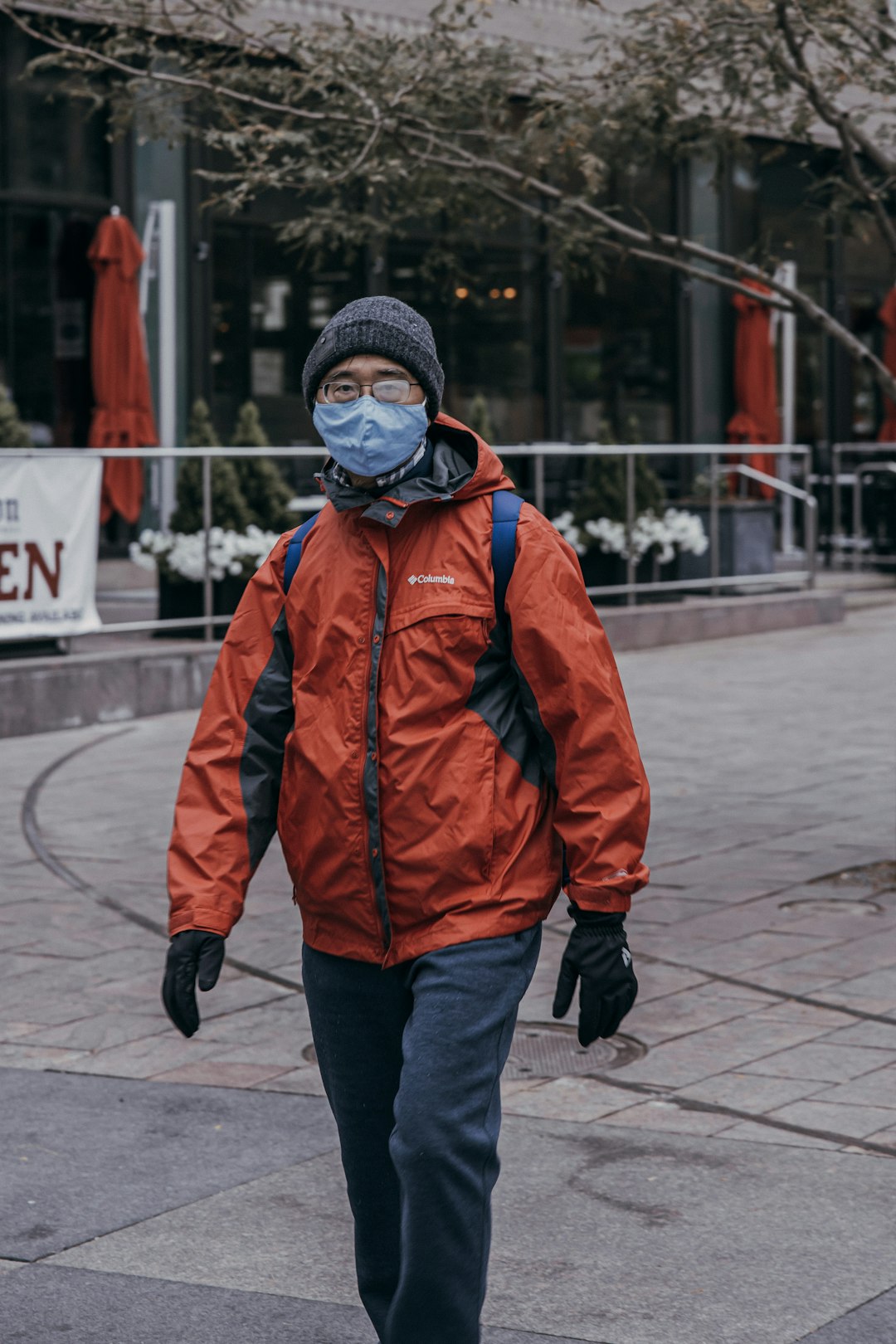 man in orange jacket and black knit cap walking on sidewalk during daytime