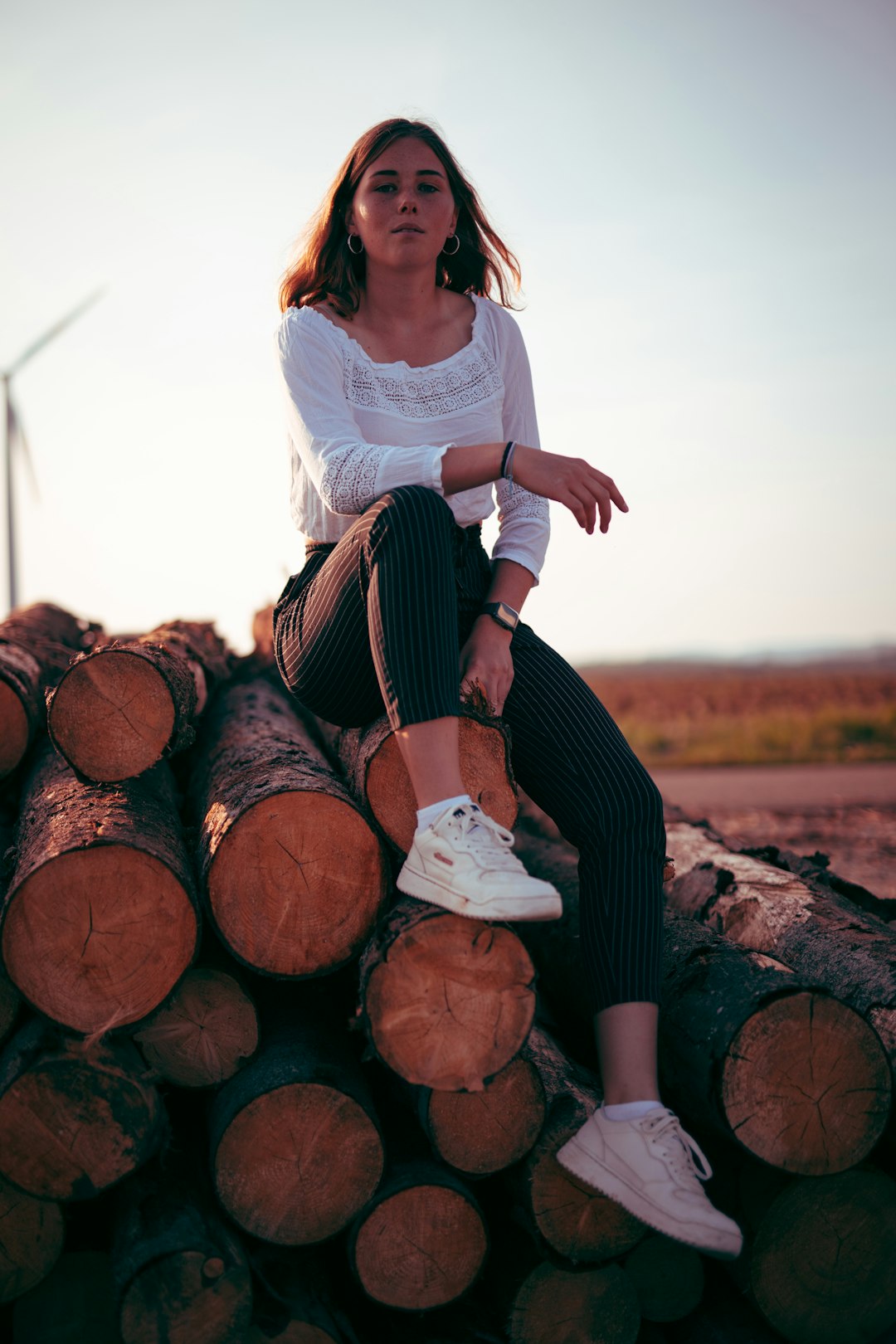 woman in white shirt and black pants sitting on brown wood log during daytime