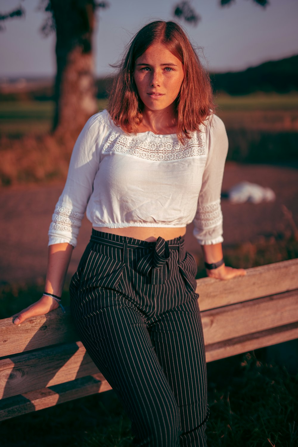 woman in white long sleeve shirt and black and white striped pants sitting on brown wooden