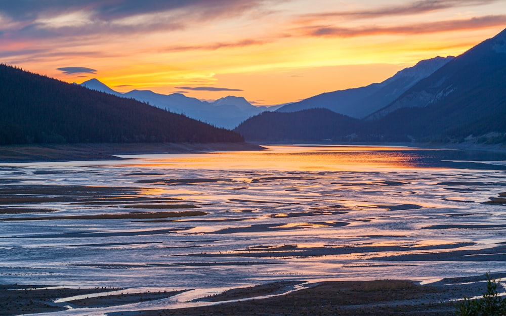 the sun is setting over a mountain lake