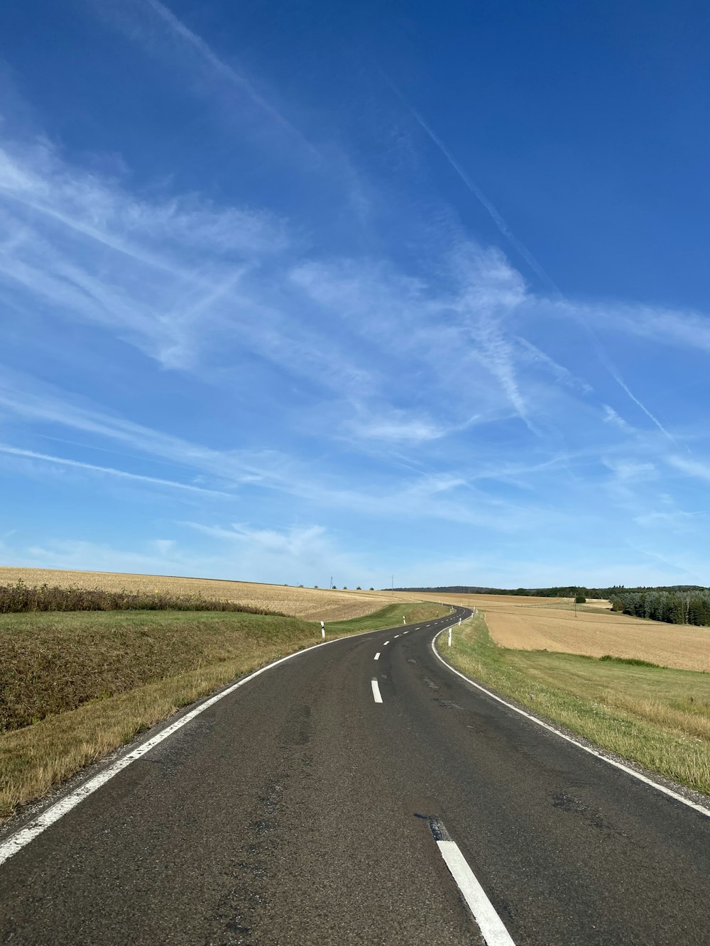 昼間の青と白の晴れた曇り空の下、緑の芝生の間の灰色のアスファルト道路