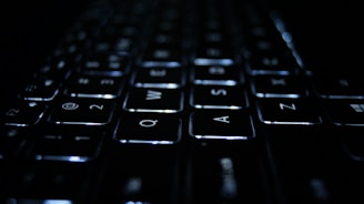 A close-up view of a keyboard with illuminated keys in a dark environment. The focus is on the Q, W, E, A, S, and D keys, which are clearly visible with soft white backlighting.