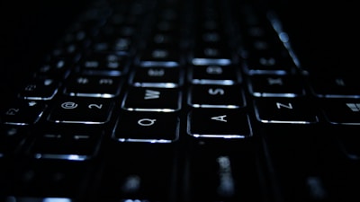 A close-up view of a keyboard with illuminated keys in a dark environment. The focus is on the Q, W, E, A, S, and D keys, which are clearly visible with soft white backlighting.