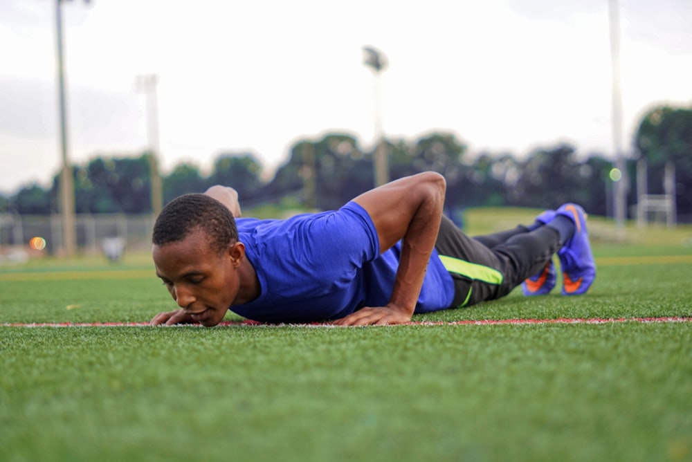 man in blue tank top lying on green grass field during daytime