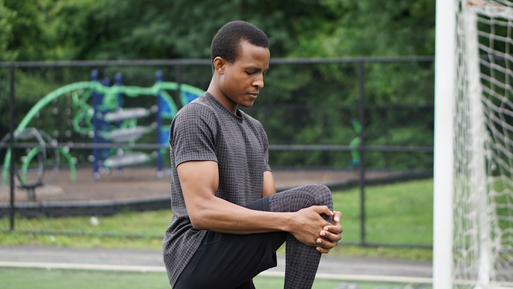 man in blue polo shirt and black pants sitting on gray concrete pavement during daytime