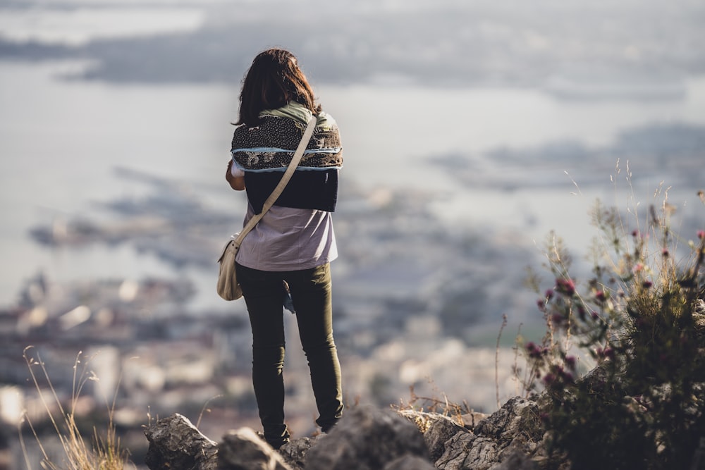 woman in brown jacket and black pants standing on rock during daytime