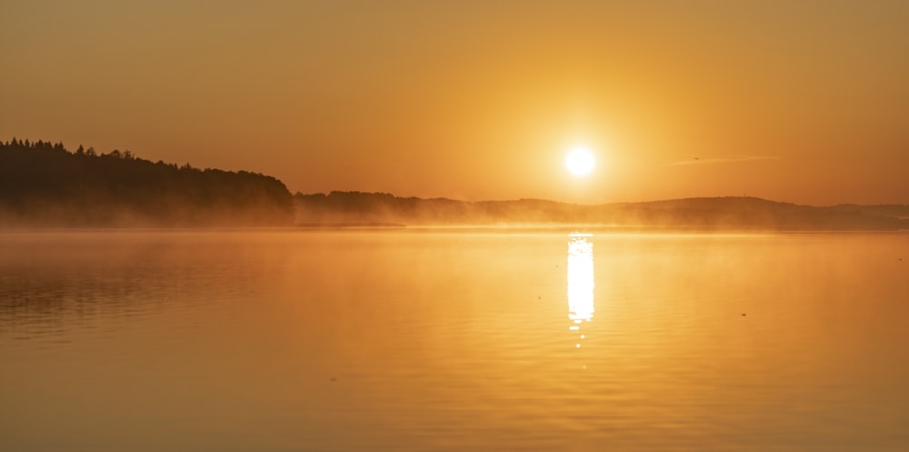 silhouette of mountain beside body of water during sunset