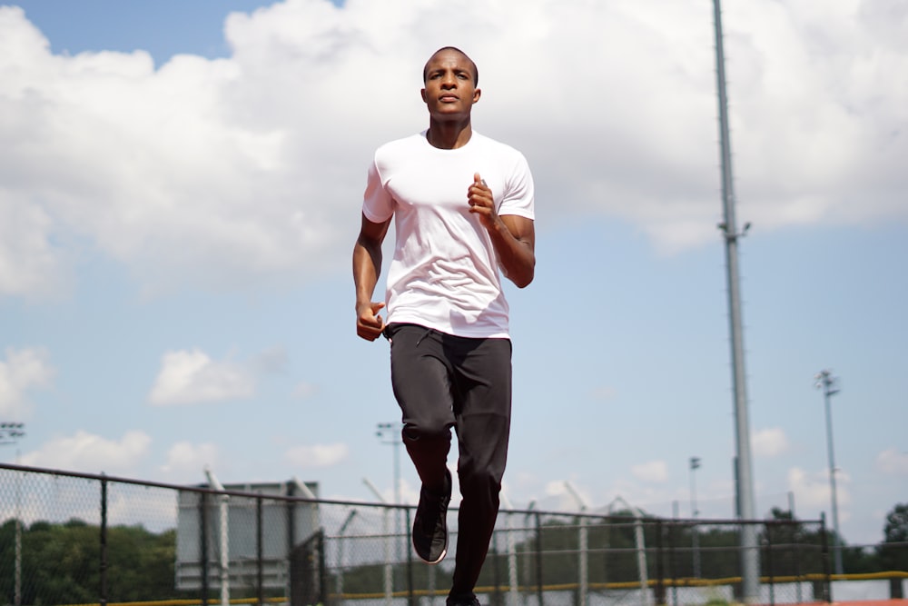 man in white crew neck t-shirt and black pants standing on field during daytime