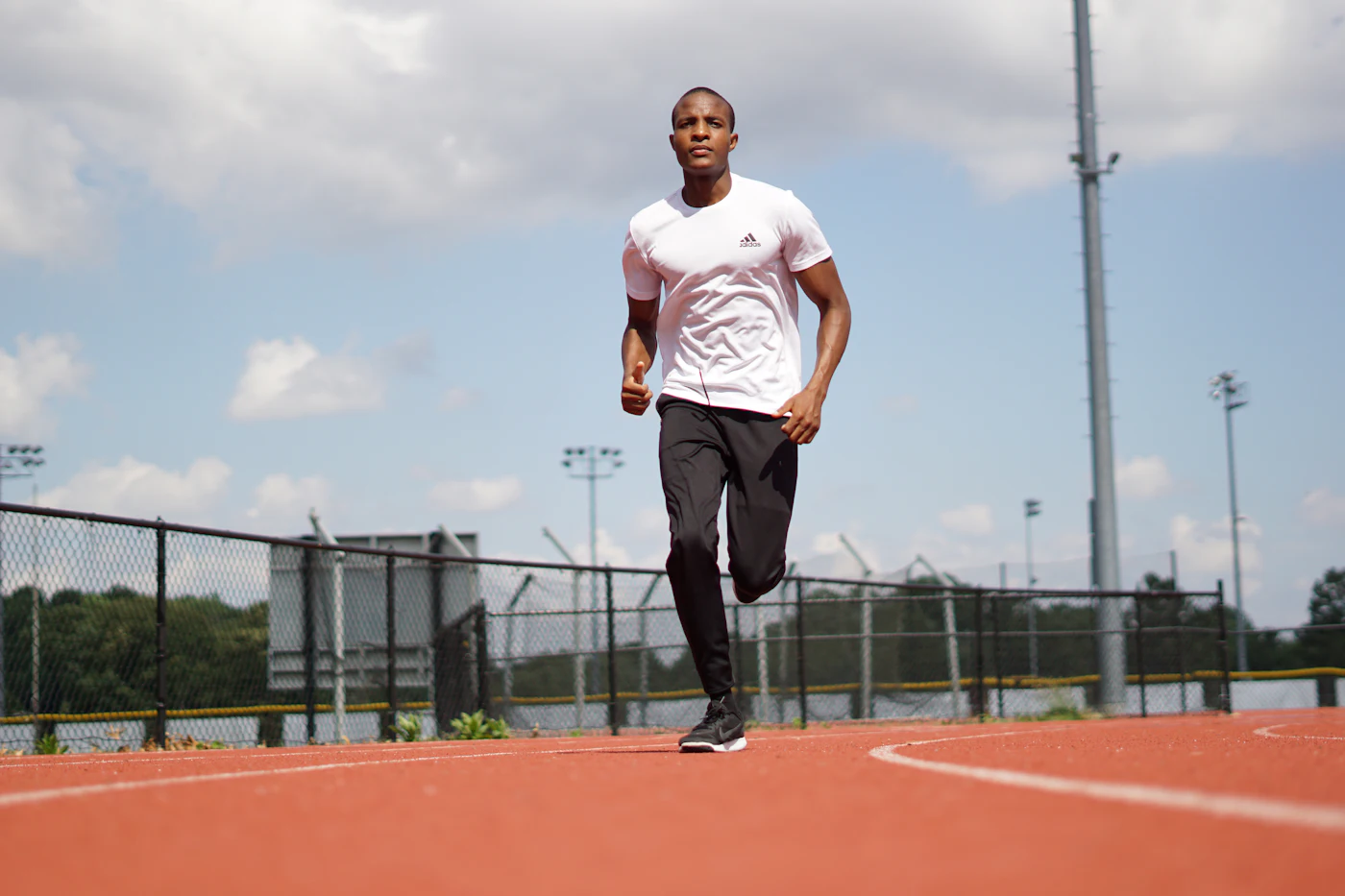 Mock photo: a Black man in a white tee mid-stride on an outdoor track. Replaced by store photography from the shoot.