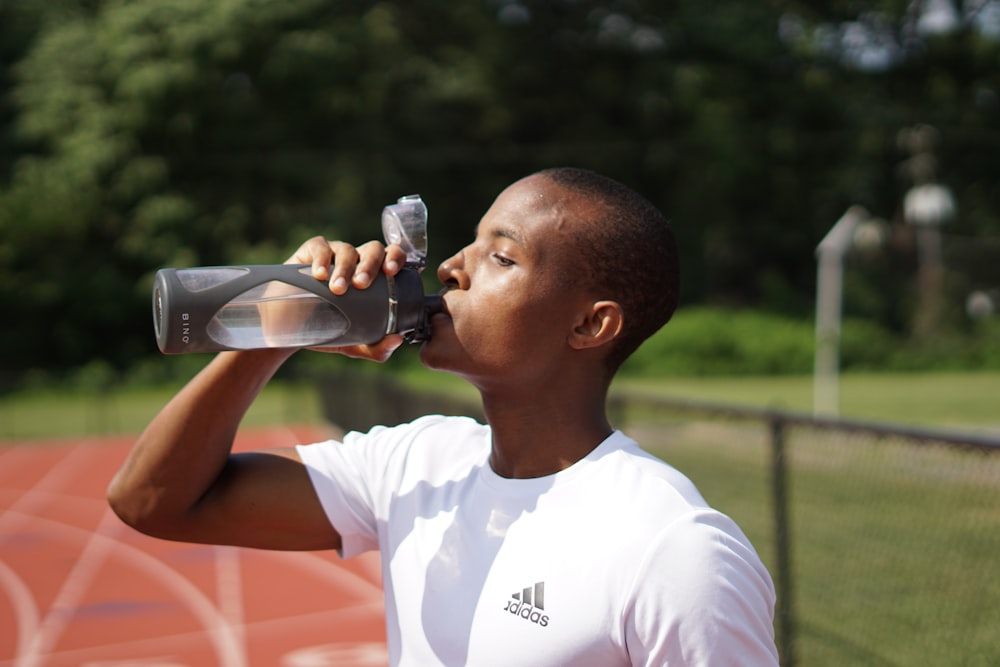 Hombre con camiseta blanca de cuello redondo bebiendo de una botella deportiva negra