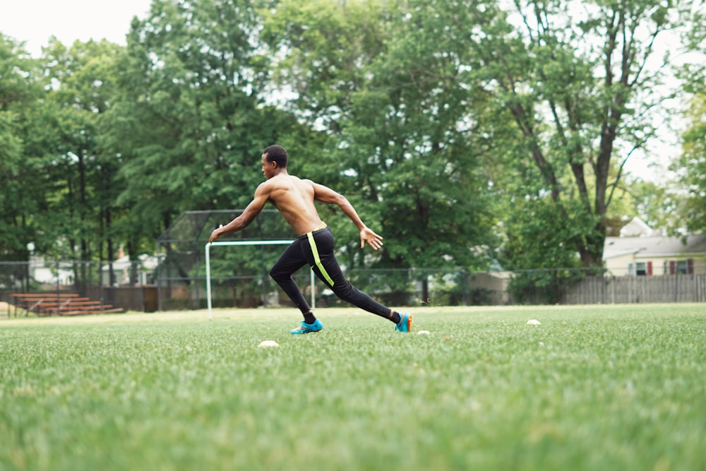 man in black shorts running on green grass field during daytime