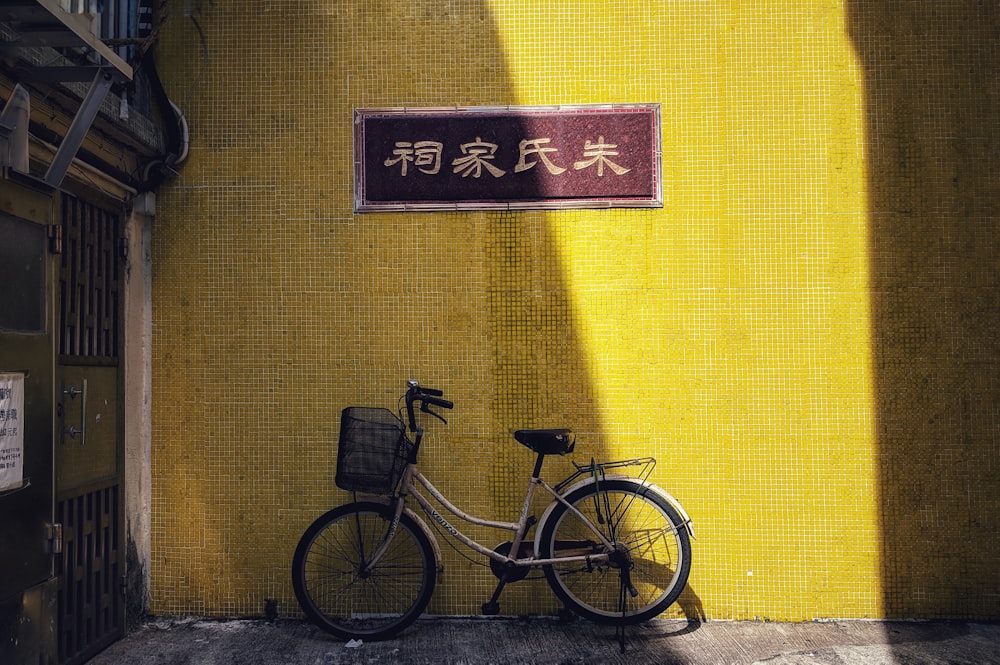 black city bicycle parked beside yellow wall