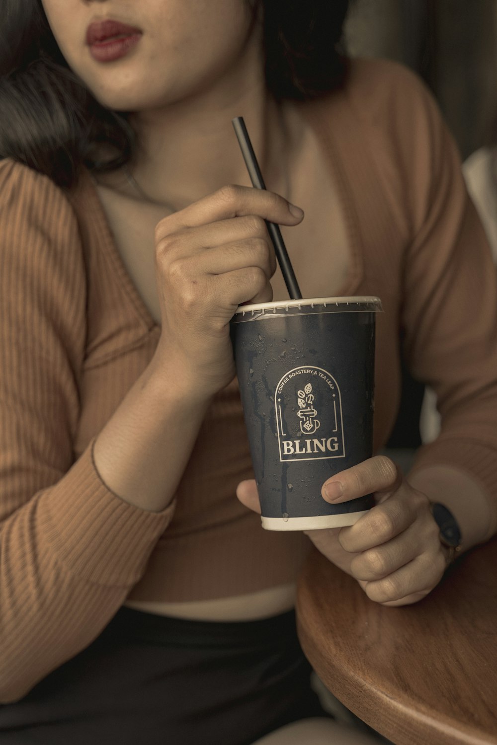 woman in brown long sleeve shirt holding black and white disposable cup