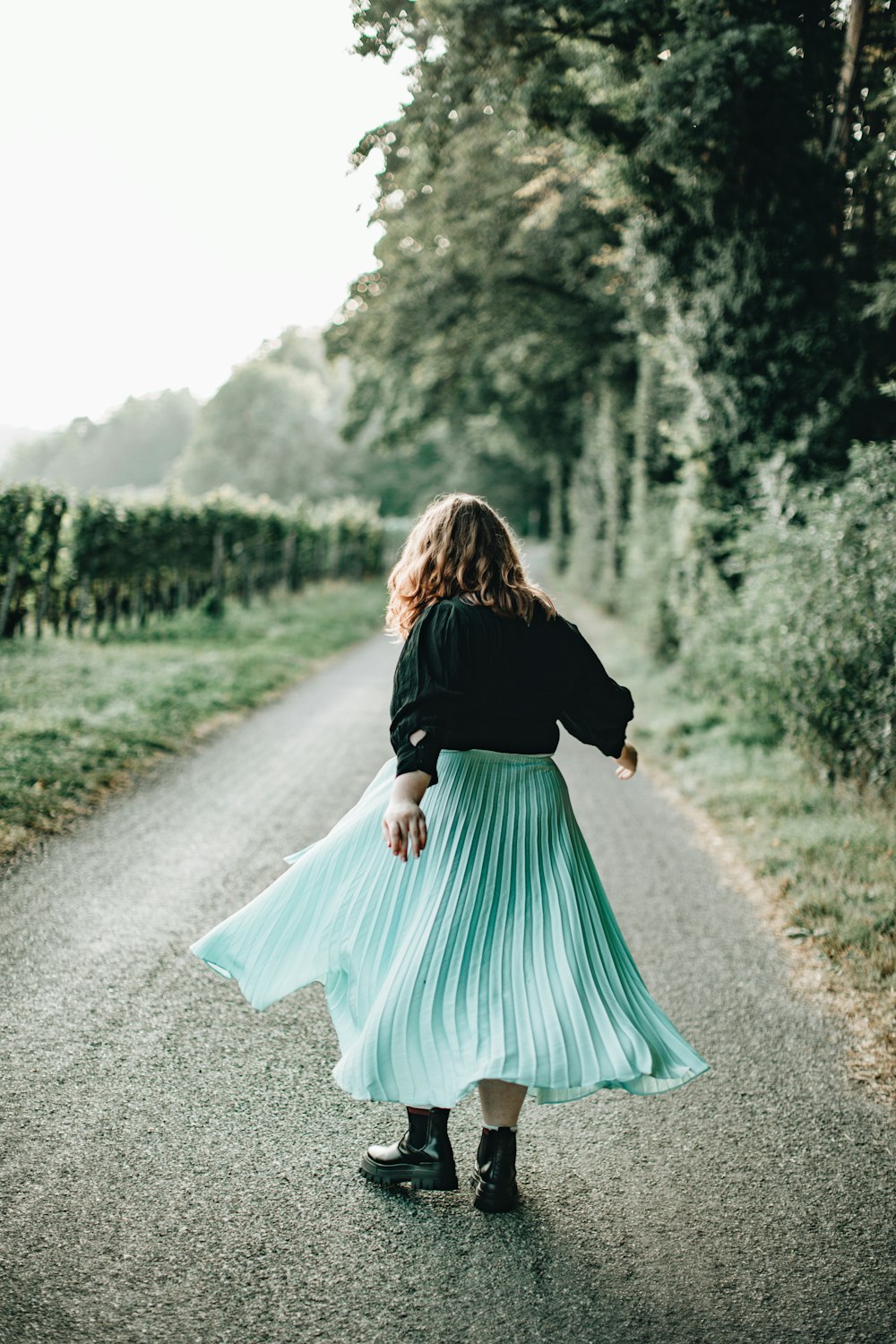 Femme en chemise noire à manches longues et jupe turquoise marchant sur un chemin de terre pendant la journée